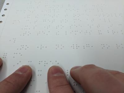 A hand reading Braille on a sheet.