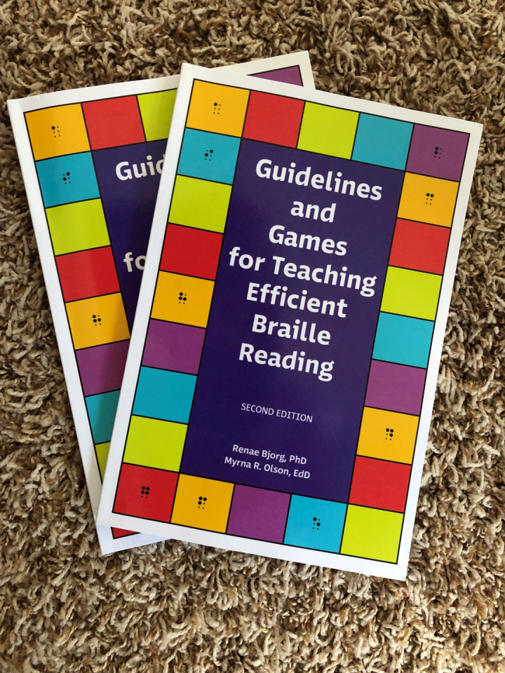2 copies of the book Guidelines and Games are fanned out. The title is in the center and colored blocks with simulated braille letters surround the perimeter of the book making it look like a game board.