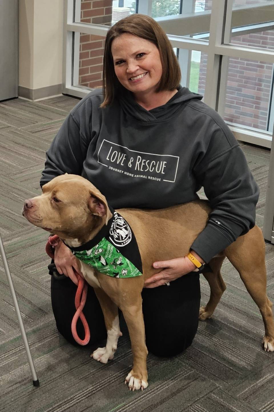 Amy smiles as she kneels next to a dog wearing a scarf.