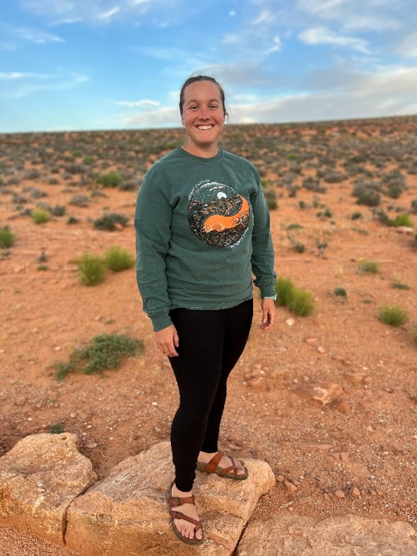 Jessica smiles while standing on a rock in the desert.