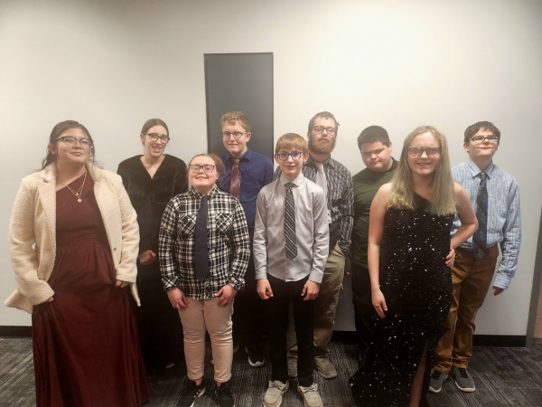 9 students wearing formal wear stand in two rows and smile at the camera.