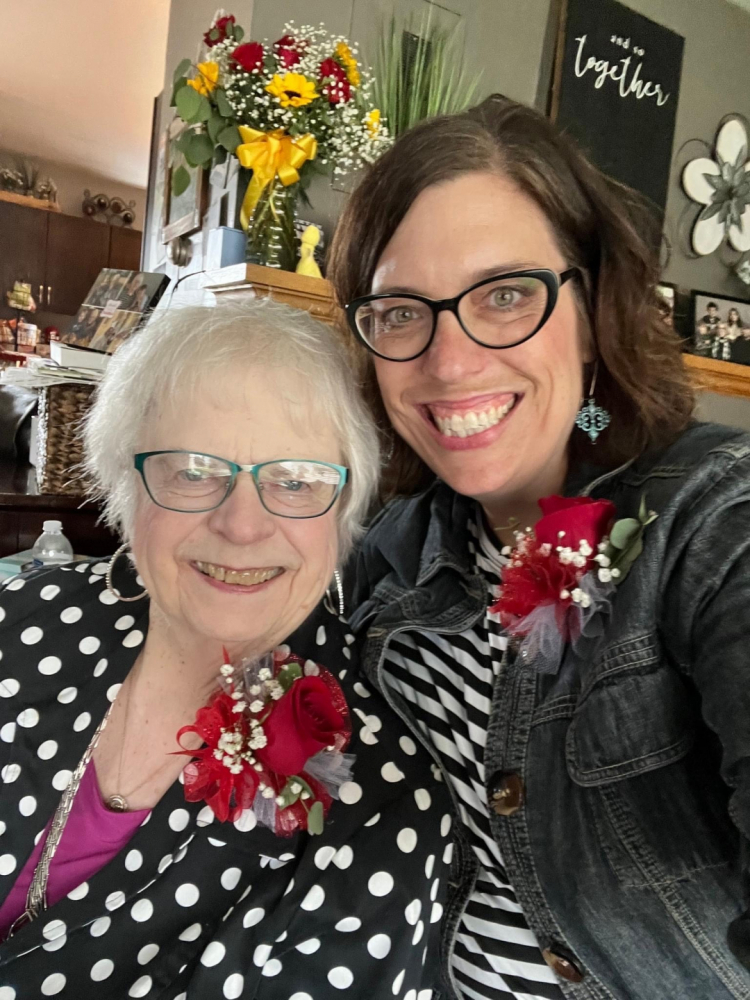 A close-up of Carmen and Amanda. Carmen is seated and Amanda, to her right, hugs her with her left arm.