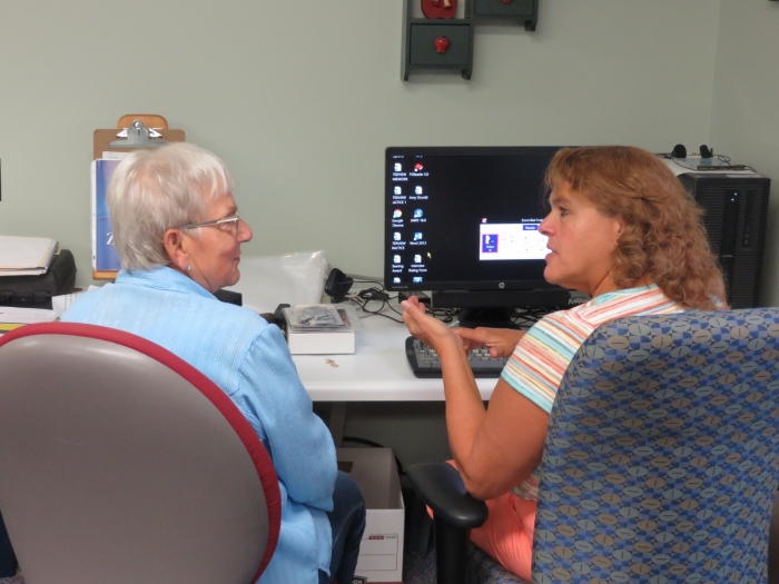 Sitting in front of a computer, an adult client listens to Assistive Tech instructor Tracy Wicken.