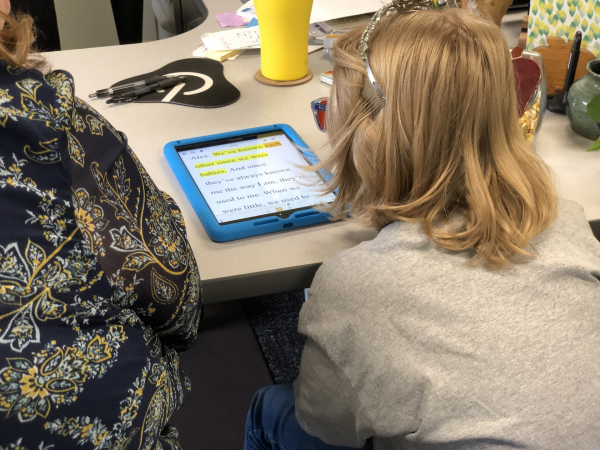 A student listens to a book being read audibly on an iPad. A word is highlighted to show which word is being read.