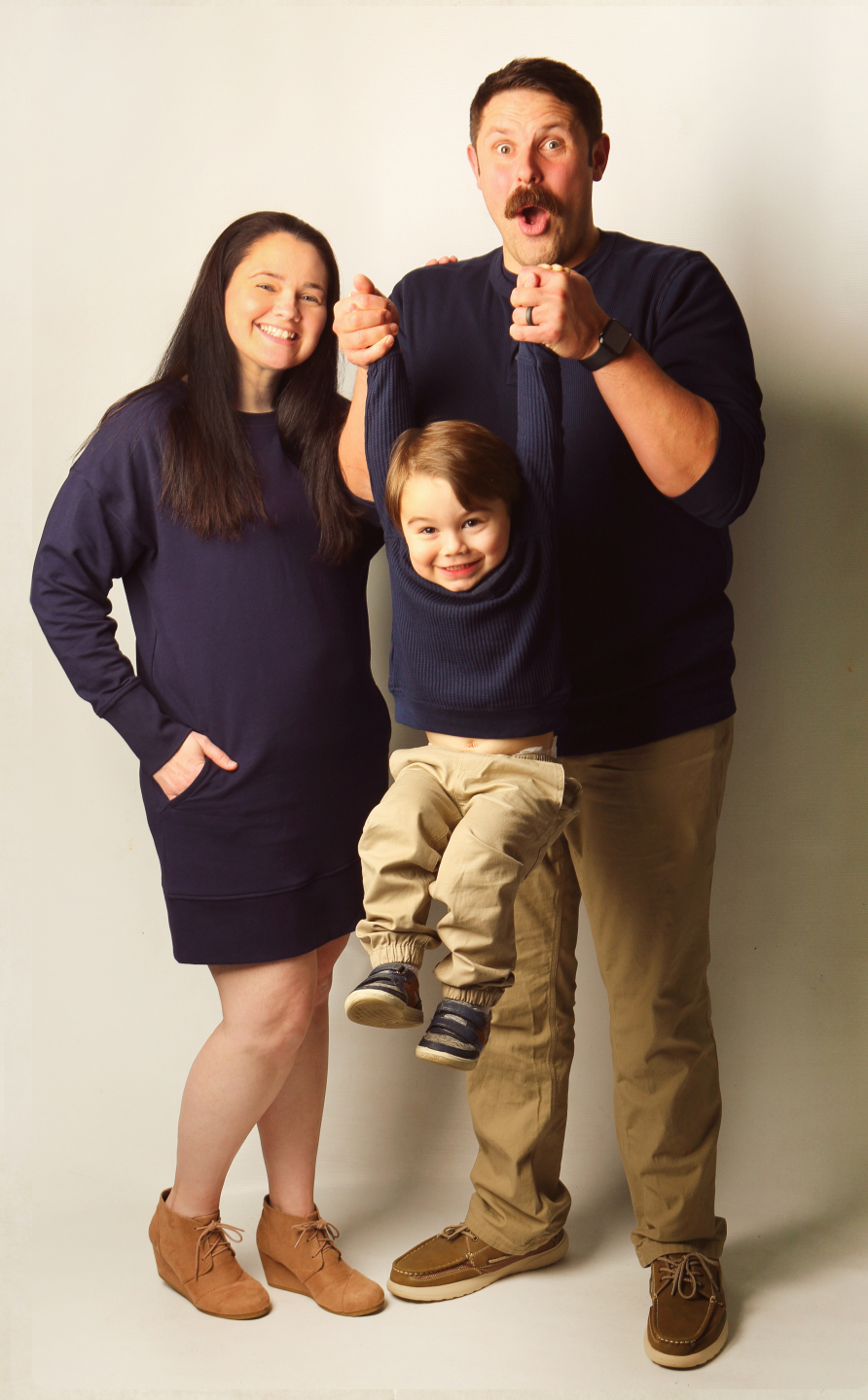 Lacey stands next to her husband Jackson who is lifting son Reuben up by the arms. Lacey and Reuben have big smiles and Jackson's mouth is open wide, as if he is surprised.