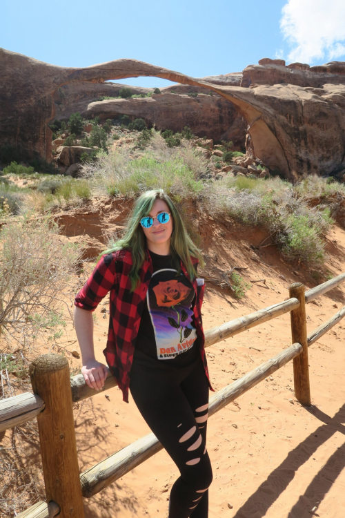 Leslie leans on a wooden fence in front of a desert scene. 