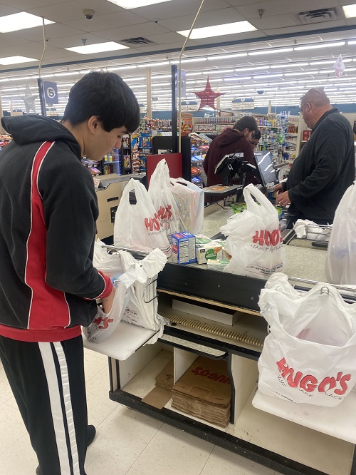 Matthew stands at the checkout bagging groceries.