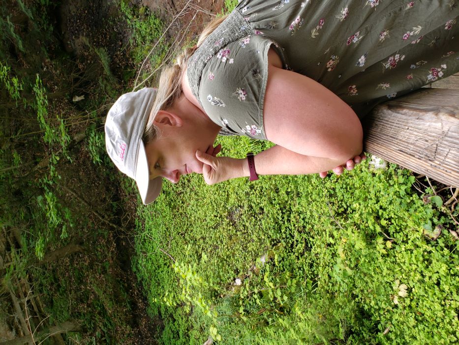 Michele leans against a fence post staring at a vista on a hike.