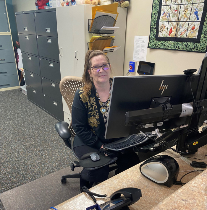 Nedra sits at her desk behind a computer. File cabinets are behind her.