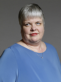 professional image of Neva Fairchild, a woman of middle age with gray hair, wearing a blue shirt and a necklace