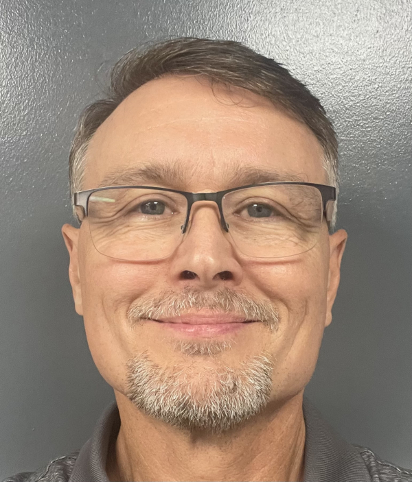 A close-up of Paul, with gray hair and a gray goatee and wearing a gray polo. He is smiling at the camera. 