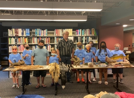 elementary students and speaker Ted stand in the library at NDVS/SB with taxidermized animals in front of them on a table.