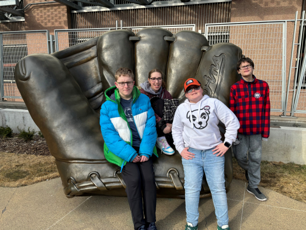 4 students sit on a statue of a baseball mit outside of Target Field.