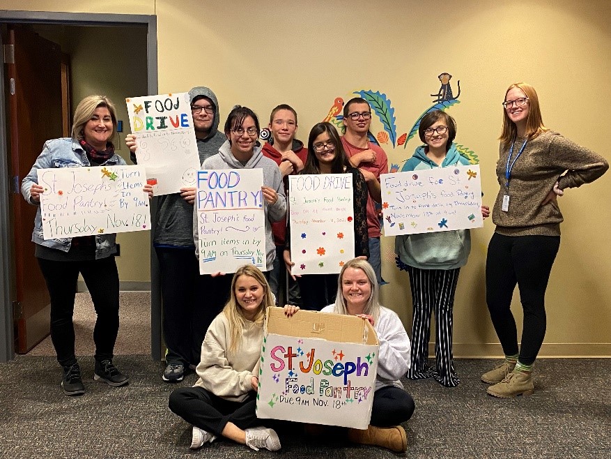 Teens, volunteers, and houseparents are lined up smiling and holding their food shelf signs.