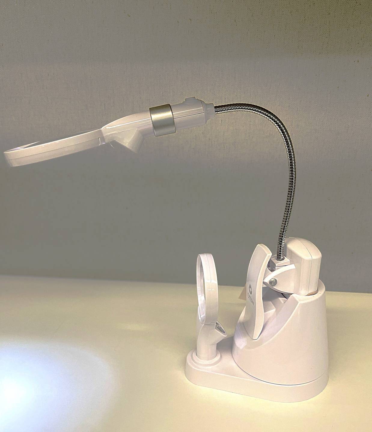 OttLite LED CLip Lamp, portable light with flexible neck and large interchangeable lighted lens, has clip on the end to attach to different surfaces or sits in a stand