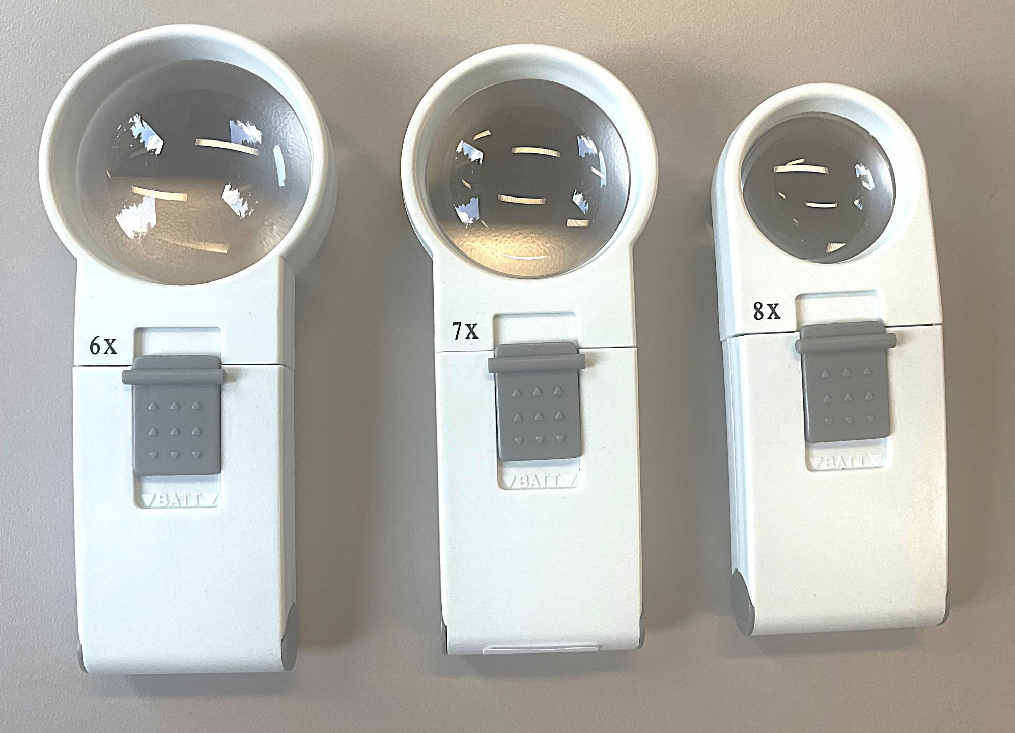 6x, 7x, and 8x magnifiers with round lenses, white handles, and gray slid buttons for illumination