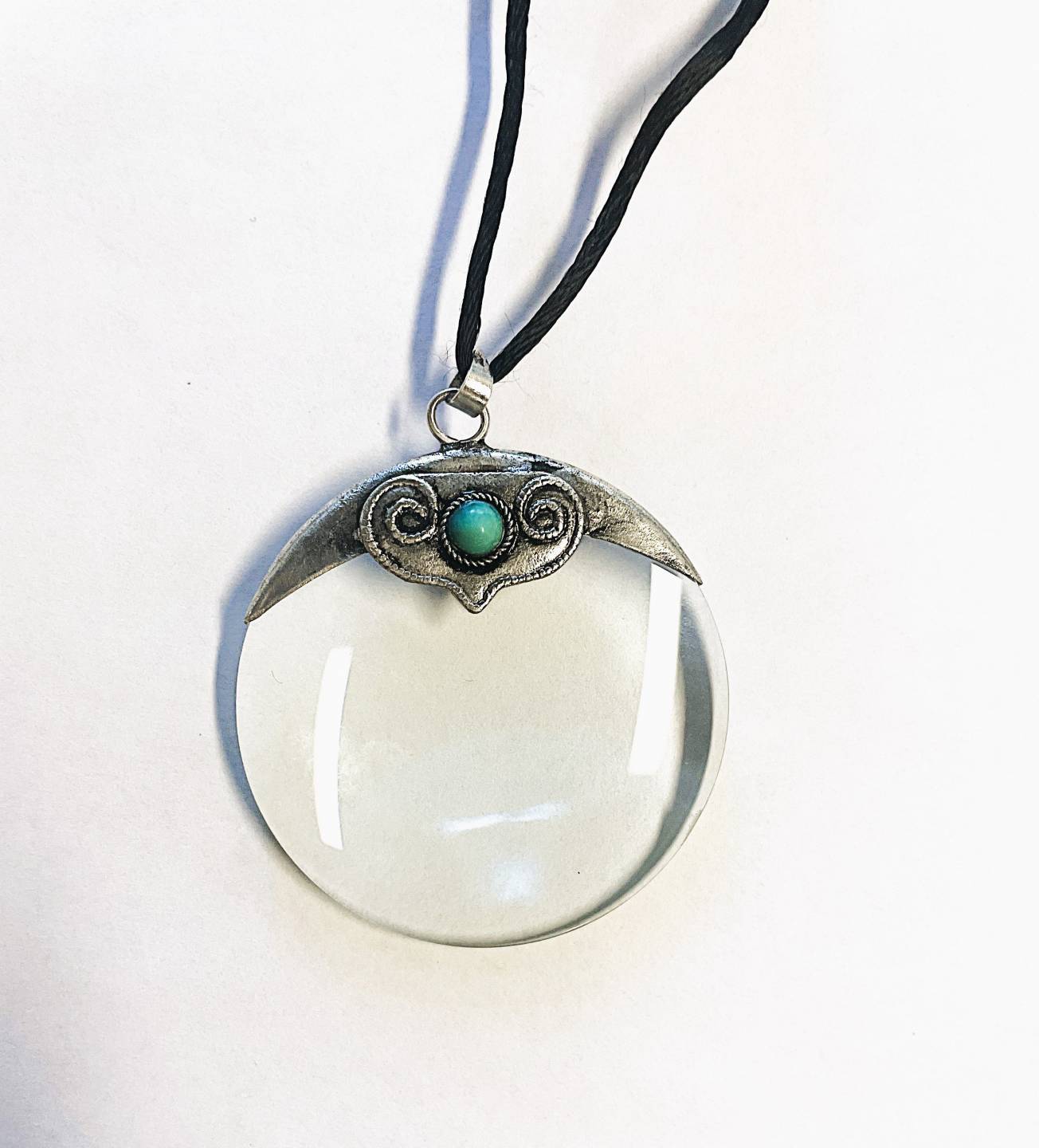 Round magnifier with silver and turquoise detailing at the top, attached to long black string to wear around the neck