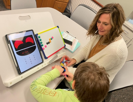 Cindy sits beside a student who is working on an iPad.