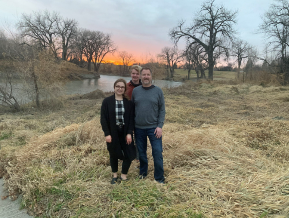 Ken with his two children outside with a river and sunset behind them.