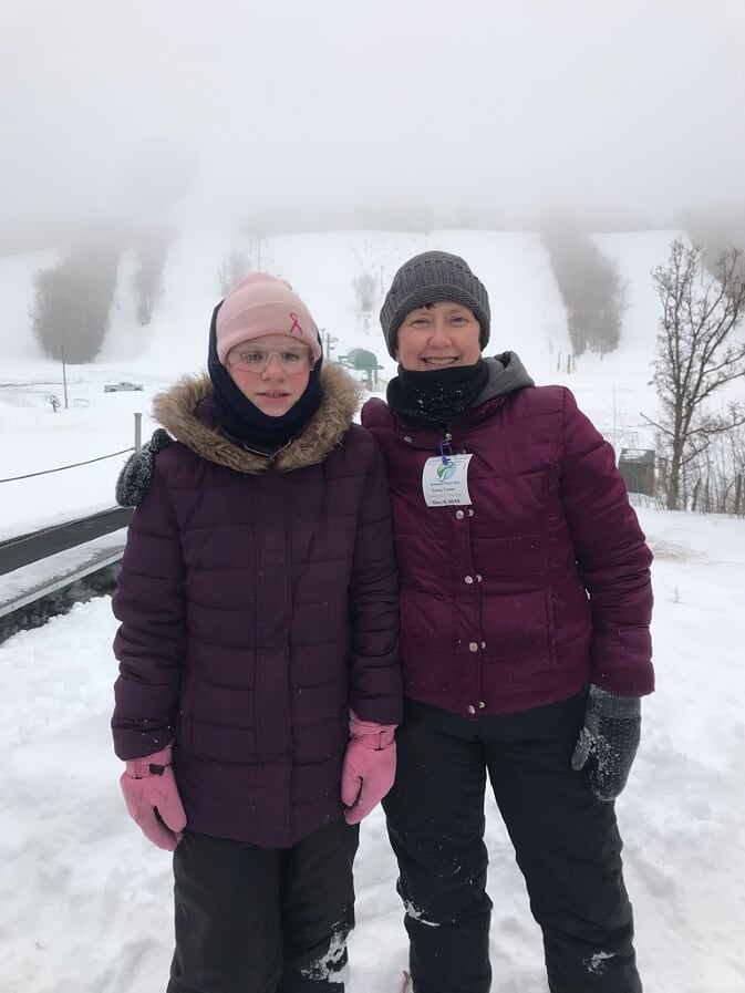 Mary stands next to a student at Annie's House in Bottineau. They are dressed to ski and are standing in the snow.