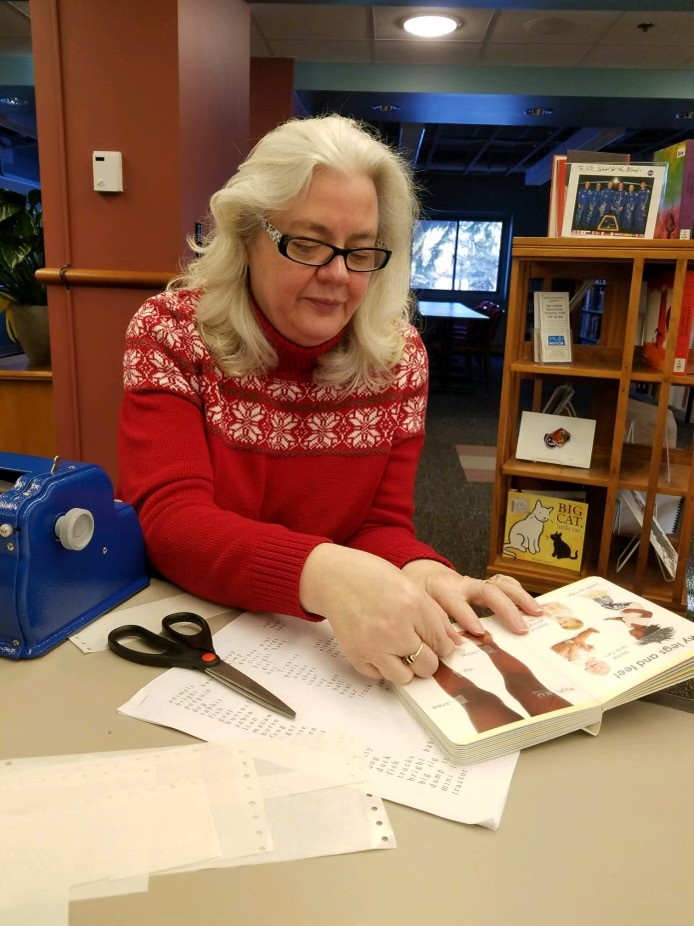 Kathy sits at a table adding braille stickers to a book for one of her students.