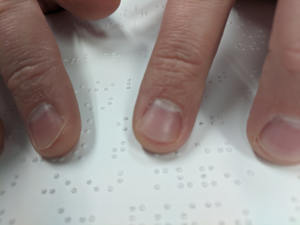Fingers reading braille on a sheet of braille paper